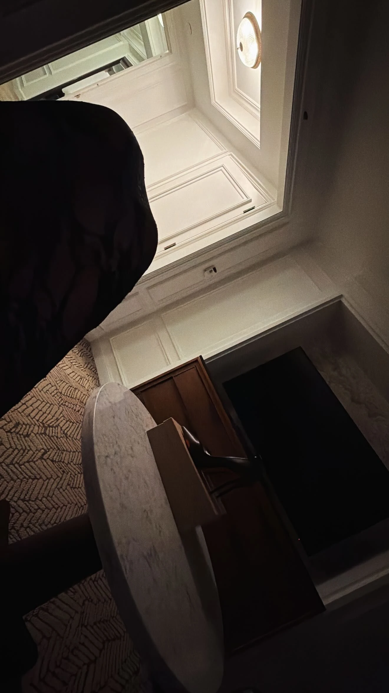 A hotel room at night, tilted: panelled walls, a marble table, a lamp.